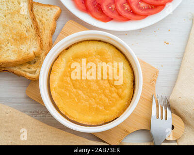 Ramequin rond blanc cuit au four avec de l'omelette les oeufs et le lait, avec une croûte, sur table en bois blanc, vue du dessus. Banque D'Images