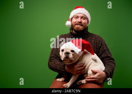 Heureux l'homme et le chien à santa caps sur fond vert en studio vide Banque D'Images