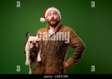 Man in santa hat avec bulldog dans les verres vides sur fond vert en studio Banque D'Images