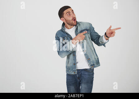 Heureux homme barbu excité dans les lunettes à la caméra avec le sourire et à l'opposé à l'espace de copie avec deux doigts isolated over white background Banque D'Images