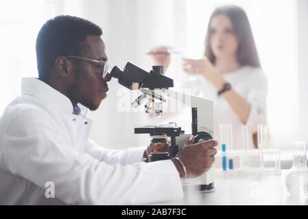 Le scientifique travaille avec un microscope dans un laboratoire effectuant des expériences et des formules. Banque D'Images