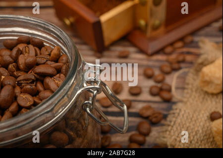 Grains de café dans un pot de verre, moulin à café, des morceaux de sucre brun sur un fond de bois. Close up Banque D'Images