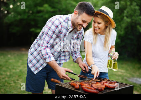 Jeune couple préparer les saucisses sur un barbecue en plein air Banque D'Images