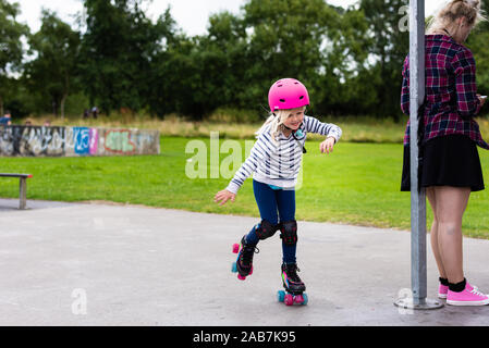 Une mignonne petite fille dans un casque rose à l'apprentissage roller skate au conseil local exécuter skate park dans la ville de Stoke on Trent Banque D'Images