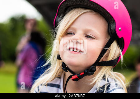 Une jolie petite fille blonde portant un casque rose tout en apprenant à roller skate, rollers, heureuse et énergique Banque D'Images