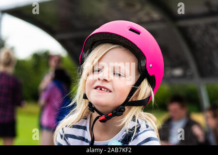 Une jolie petite fille blonde portant un casque rose tout en apprenant à roller skate, rollers, heureuse et énergique Banque D'Images