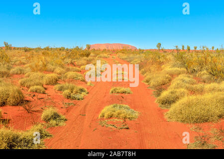 Chemin de sable rouge sec en paysage de brousse en Australie avec Ayers Rock au loin, le Parc National d'Uluru-Kata Tjuta, l'UNESCO, de l'Australie Banque D'Images