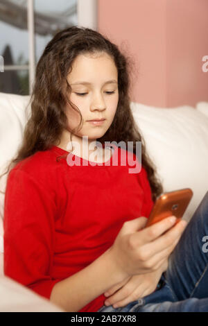 Ein junges Maedchen auf dem canapé, mit einem Mobiltelefon in der Hand Banque D'Images