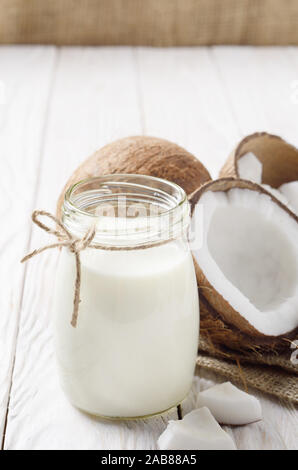 Pot Mason de lait ou de yogourt sur le chanvre serviette sur une table en bois blanc à la noix de coco de côté Banque D'Images