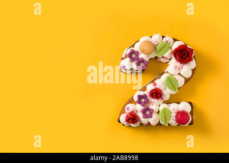 Numéro deux gâteau décoré de fleurs et de macarons isolé sur fond jaune. Copy space Banque D'Images