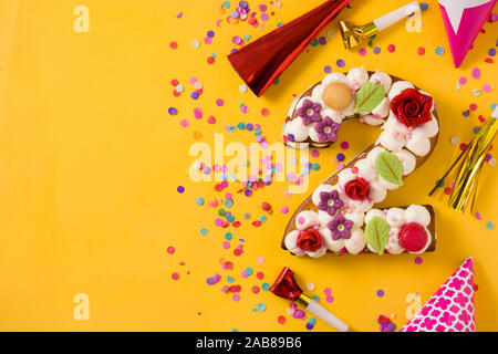 Numéro deux gâteau décoré de fleurs macarons et confettis isolé sur fond jaune. Copy space Banque D'Images