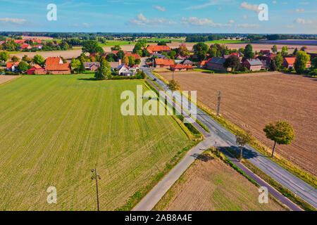 Vue aérienne d'une route de campagne menant à un village dans un paysage culturel de la monotonie des terres arables. Banque D'Images