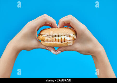 Femme mains tenant un burger sur un fond bleu. Deux mains faisant signe coeur avec hamburger Banque D'Images