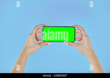 Femme hands holding smartphone avec un écran vert sur un fond bleu. Mock de mobile Banque D'Images