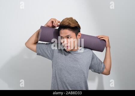 Fitness homme asiatique avec un tapis de yoga debout sur fond blanc Banque D'Images