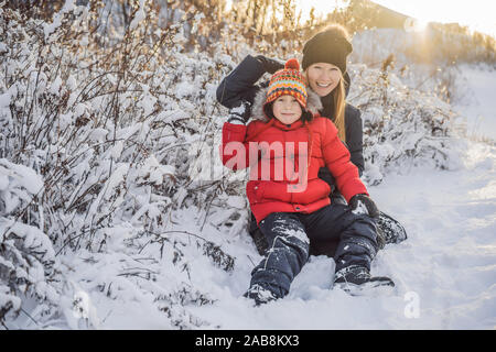 La mère et le fils d'hiver boule de jeter l'appareil photo à smiling happy s'amuser en plein air, sur l'enneigement de l'hiver journée à jouer dans la neige. Jolie jeune femme espiègle Banque D'Images