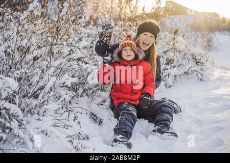 La mère et le fils d'hiver boule de jeter l'appareil photo à smiling happy s'amuser en plein air, sur l'enneigement de l'hiver journée à jouer dans la neige. Jolie jeune femme espiègle Banque D'Images