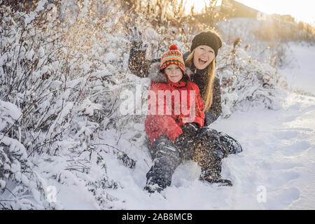 La mère et le fils d'hiver boule de jeter l'appareil photo à smiling happy s'amuser en plein air, sur l'enneigement de l'hiver journée à jouer dans la neige. Jolie jeune femme espiègle Banque D'Images