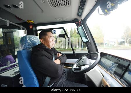 Un superviseur de sécurité chinois a les bras croisés sur la chese pendant qu'il observe la situation sur un 5G en fonctionnalités de conduite auto-minibus sur la route en cours d'exécution Banque D'Images