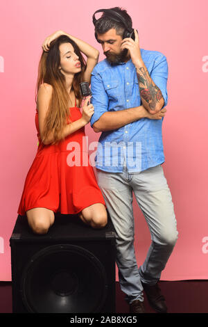 Homme avec barbe porte un casque. Couple dans l'amour est assis sur le haut-parleur sur fond rose. Guy avec barbe et dame avec visages détendue d'écouter de la musique. La musique et les loisirs concept. Banque D'Images