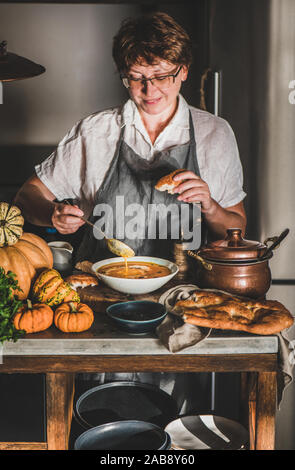 Femme en tablier gris la cuisson et dégustation de soupe au potiron Banque D'Images