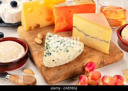 Plateau de fromages. Fromage bleu, rouge Leicester, Brie, Emmental et d'autres avec du vin et du raisin sur un fond blanc Banque D'Images