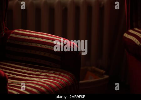 Fauteuils à rayures d'or rouge sur fond de batterie de chauffage dans une pièce sombre. Banque D'Images