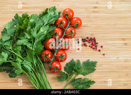 Légumes frais sur la table, copiez l'espace. Arrière-plan de l'alimentation. Mise à plat. Les tomates cerises, un bouquet de persil, poivron rouge et noir sur une planche à découper en bois Banque D'Images