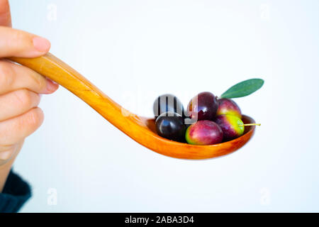 Une femme poignée d'olives de la Méditerranée sur une cuillère en bois isolé sur fond blanc Banque D'Images