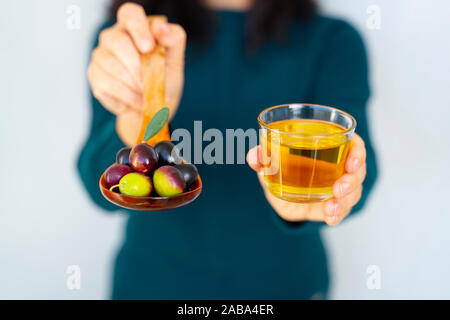 Une femme poignée d'olives de la Méditerranée sur une cuillère en bois et d'huile d'olive sur fond blanc isolé Banque D'Images