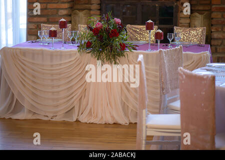 De belles roses rouges frais et de verdure centre situé sur une table de fête avec des verres et des bougies et drapée dans un voile soyeux Banque D'Images