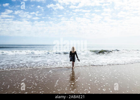 Une femme de patauger dans le surf sur Ocean City beach holding ses sandales dans il part, Ocean City, Maryland, USA. Banque D'Images