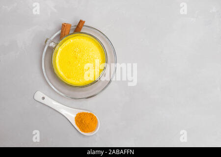 Le curcuma anti-inflammatoires dans un verre de lait golden cup avec des bâtons de cannelle et poudre de curcuma sur table béton gris Banque D'Images