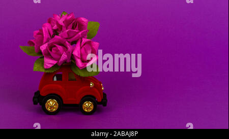 Sochi, Russie - 26 octobre 2019 : velours rouge petite voiture livrer bouquet de fleurs sur fond violet avec copie espace. Carte de Saint-Valentin, birthda Banque D'Images