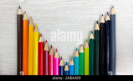 Série de crayons de couleur sur un fond de bois blanc placés de manière à dessiner une courbe Banque D'Images