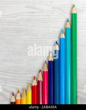 Série de crayons de couleur sur un fond de bois blanc placés de manière à dessiner un graphique de croissance exponentielle Banque D'Images