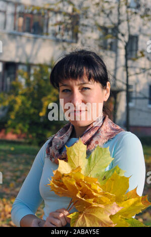 Jolie belle femme dans les vêtements de feuilles d'automne jaune tient dans ses mains sur l'arrière-plan de pâtés Banque D'Images