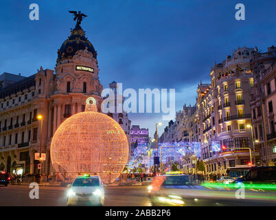 La rue Gran Via à la tombée de la nuit éclairée par les lumières de Noël et une brillante boule de noël. Vue depuis la rue Alcala. Banque D'Images