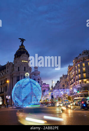 La rue Gran Via à la tombée de la nuit éclairée par les lumières de Noël et une brillante boule de noël. Vue depuis la rue Alcala. Banque D'Images