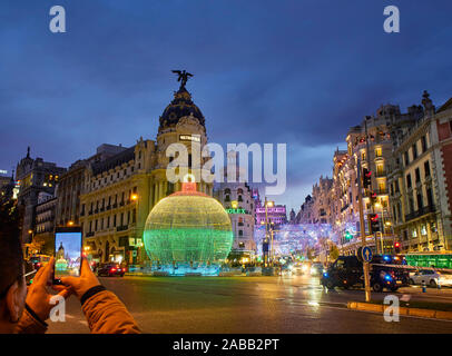 La rue Gran Via à la tombée de la nuit éclairée par les lumières de Noël et une brillante boule de noël. Vue depuis la rue Alcala. Banque D'Images