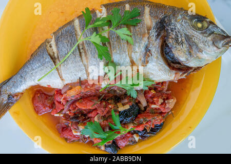 Poissons daurade cuit entier à la tomate et persil garnir joliment servi sur une assiette. Banque D'Images