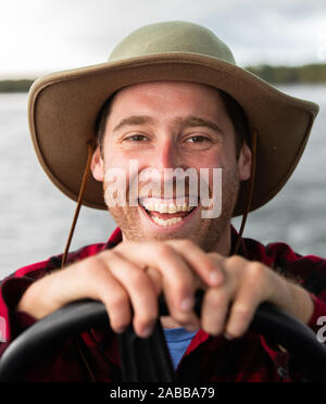 Jeune homme avec chapeau conduisant un bateau disant qu'il est facile de l'air cool dans ce bateau Banque D'Images