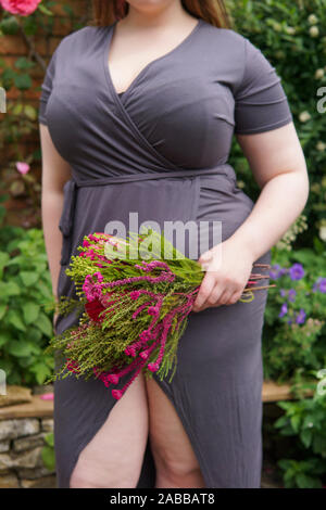 Femme debout dans un jardin tenant un bouquet de fleurs, England, UK Banque D'Images