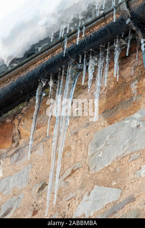 Glaçons pendant de gouttières sur un mur de pierre Banque D'Images