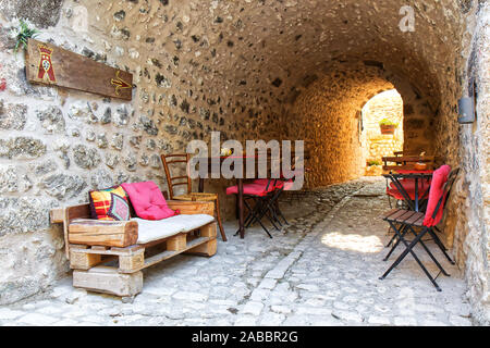 Santo Stefano di Sessanio, allée pavées étroites avec une table en bois, tables, chaises et coussins rouges Banque D'Images