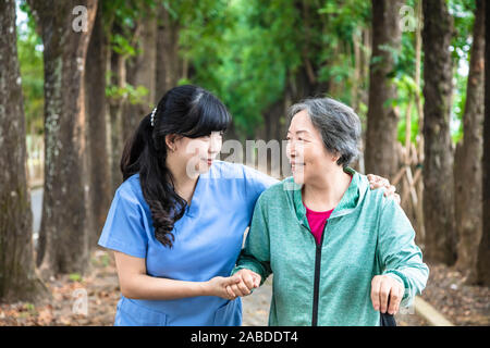 Smiling nurse helping senior woman de marcher autour du parc Banque D'Images