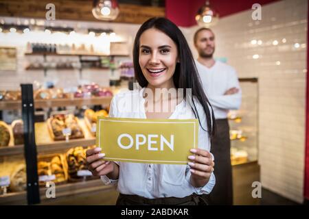 Woman holding open sign lors de l'ouverture à la pâtisserie avec mari Banque D'Images