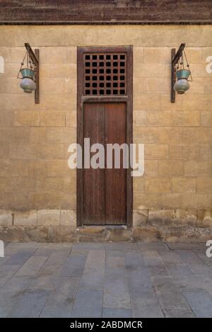 Porte fermée en bois et verre arabe deux lanternes rue pendus sur un poteau en bois dans le vieux mur de briques en pierre médiévale, Le Caire, Égypte Banque D'Images