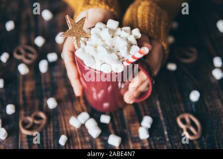 Femme en pull jaune holding mug de chocolat chaud recouvert de guimauve sur fond de bois sombre. Banque D'Images