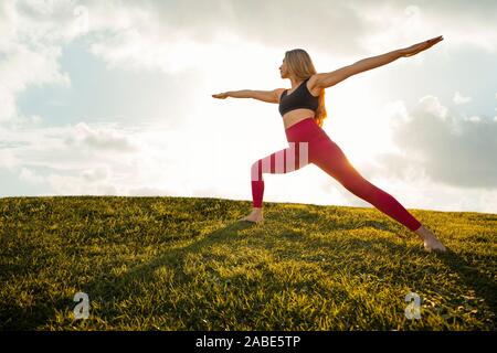 Belle femme l'exercice de Yoga Asana 2 Guerrier Pose tranquille Position Coucher du Soleil - Silhouette Isolated Background Banque D'Images